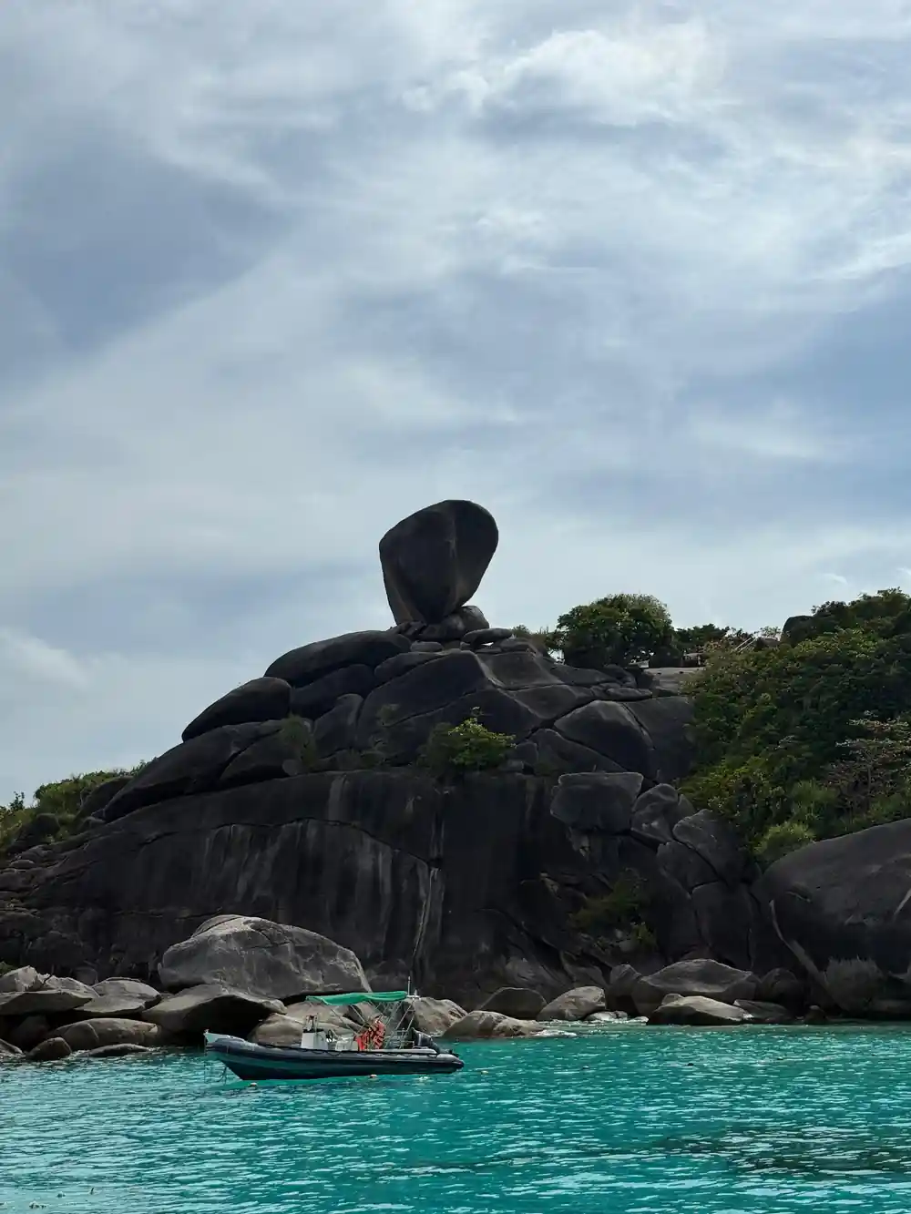 Large black rock formation rising from turquoise sea