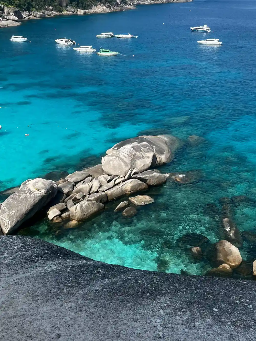 Large granite boulders in clear turquoise water with boats