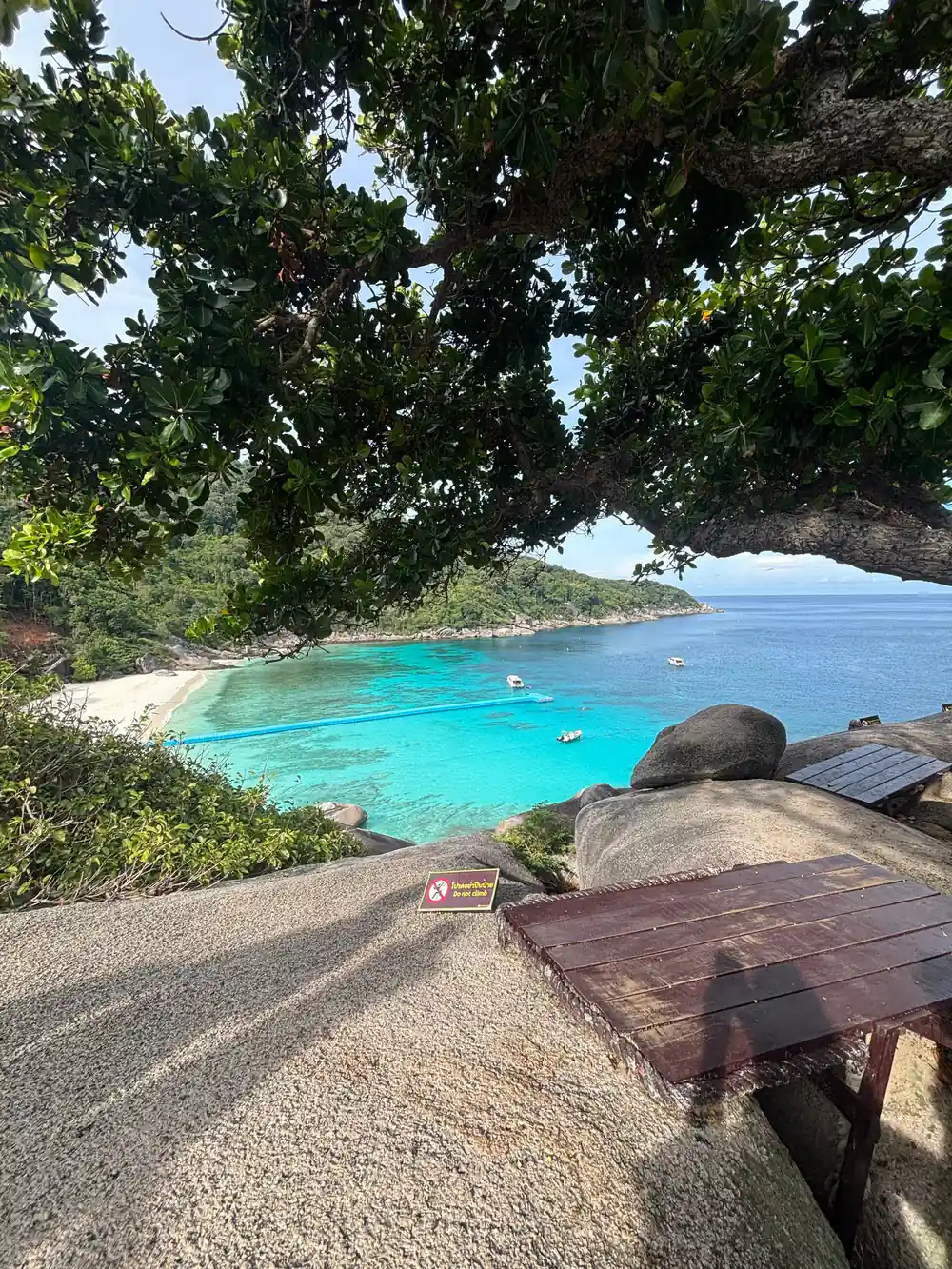 Turquoise bay with boats, rocks, and forested shoreline from wooden deck