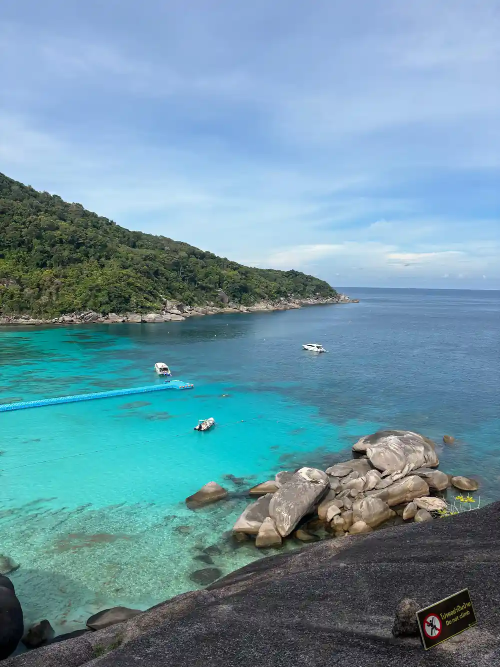 Turquoise bay with multiple boats and forested hillside from elevated viewpoint